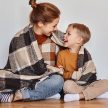 Eine Mutter und ihr Sohn kuscheln sich in eine Decke und schauen sich glücklich an.