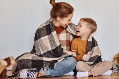 Eine Mutter und ihr Sohn kuscheln sich in eine Decke und schauen sich glücklich an.