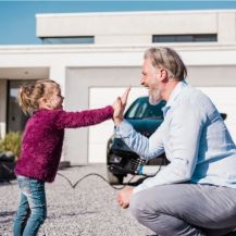 Ein Mädchen gibt ihrem Vater vor dem E-Auto ein High Five.