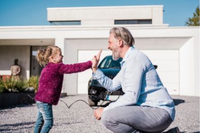 Ein Mädchen gibt ihrem Vater vor dem E-Auto ein High Five.