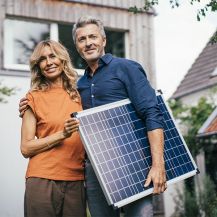 Ein Ehepaar steht vor seinem Haus mit einem Solarpanel in den Händen.