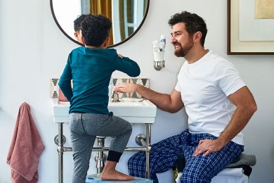 Vater und Sohn stehen gemeinsam im Badezimmer vor einem Waschbecken.