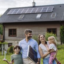 Eine junge Familie vor Ihrem Haus mit Solarpanelen auf dem Dach. 