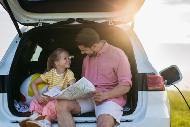 Vater und Tochter sitzen im Kofferraum eines E-Autos, das aufgeladen wird.