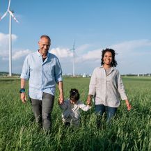 Familie läuft durch ein Feld, im Hintergrund sind Windräder zu sehen.