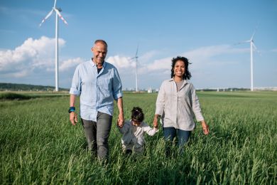 Familie läuft durch ein Feld, im Hintergrund sind Windräder zu sehen.