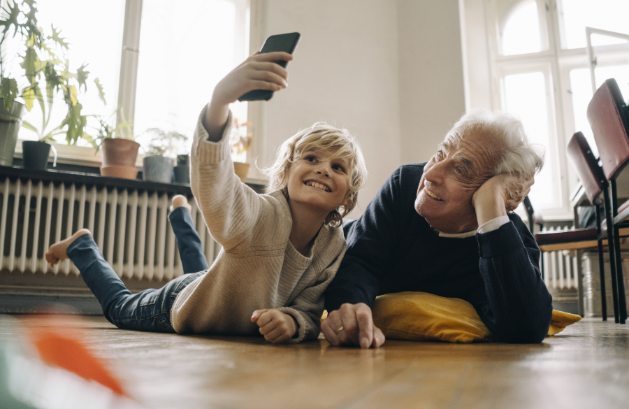 Großvater und Enkel liegen auf dem Fußboden und machen mit dem Handy ein Selfie.