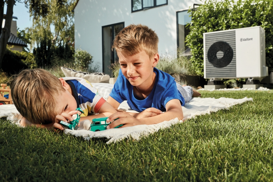 Zwei Jungen spielen im Garten auf einer Decke, im Hintergrund steht eine Wärmepumpe.