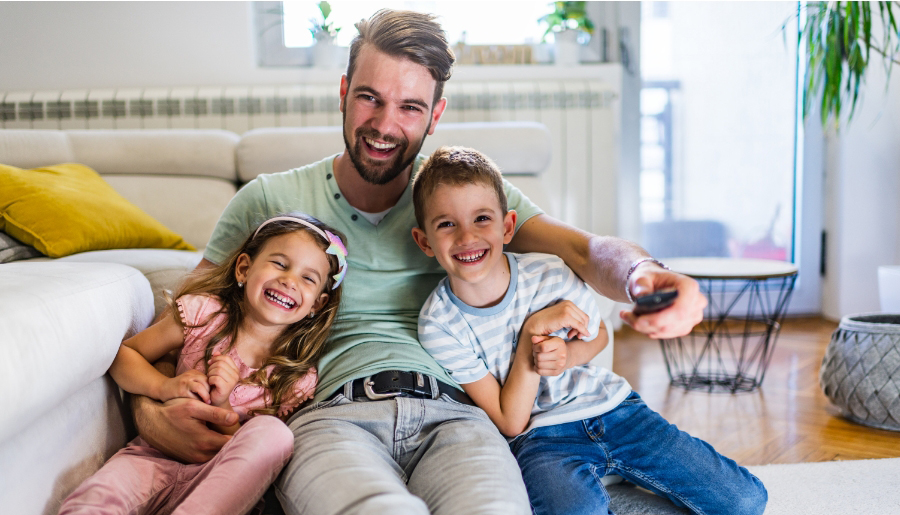 Ein Vater und seine zwei kleinen Kindern sitzen zusammen auf dem Sofa und sehen fern.